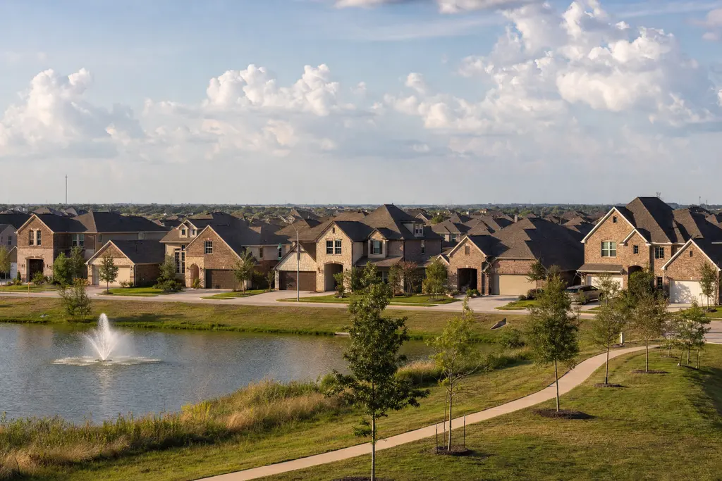 Row of two-story brick homes along a retention pond with a fountain and a walking trail at the edge of the prairie